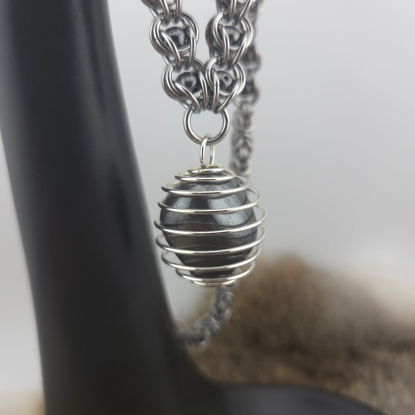 A stainless steel chainmail necklace with a steel spiral wrapped hematite pendant, handwoven.