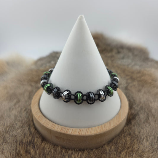 A barrel weave chainmail bracelet in the agender pride flag colors of green, black, gray, and silver.