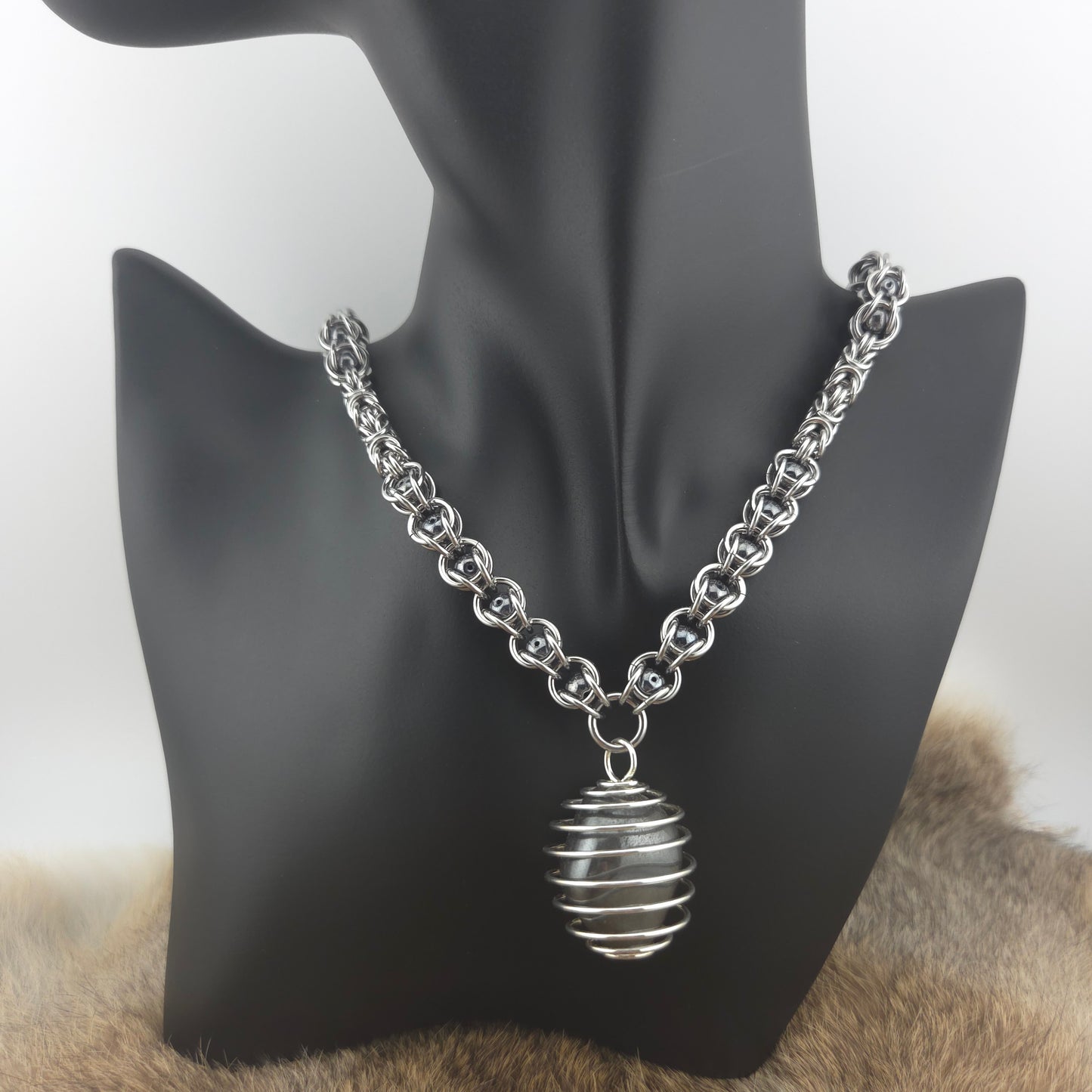 A stainless steel chainmail necklace with a steel spiral wrapped hematite pendant, handwoven.