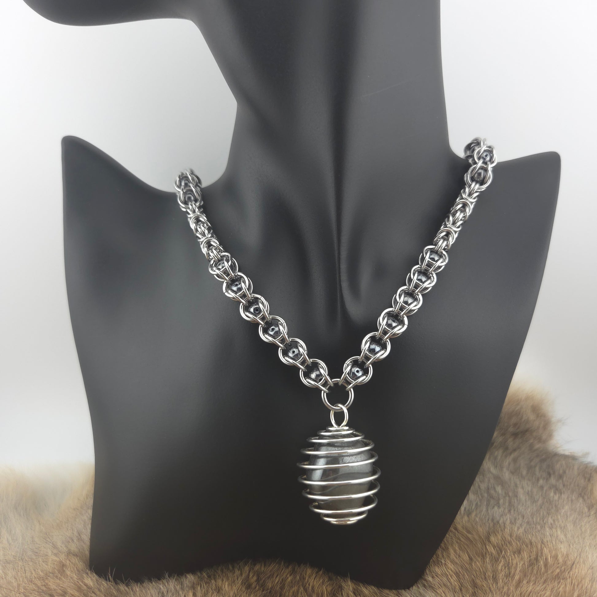 A stainless steel chainmail necklace with a steel spiral wrapped hematite pendant, handwoven.