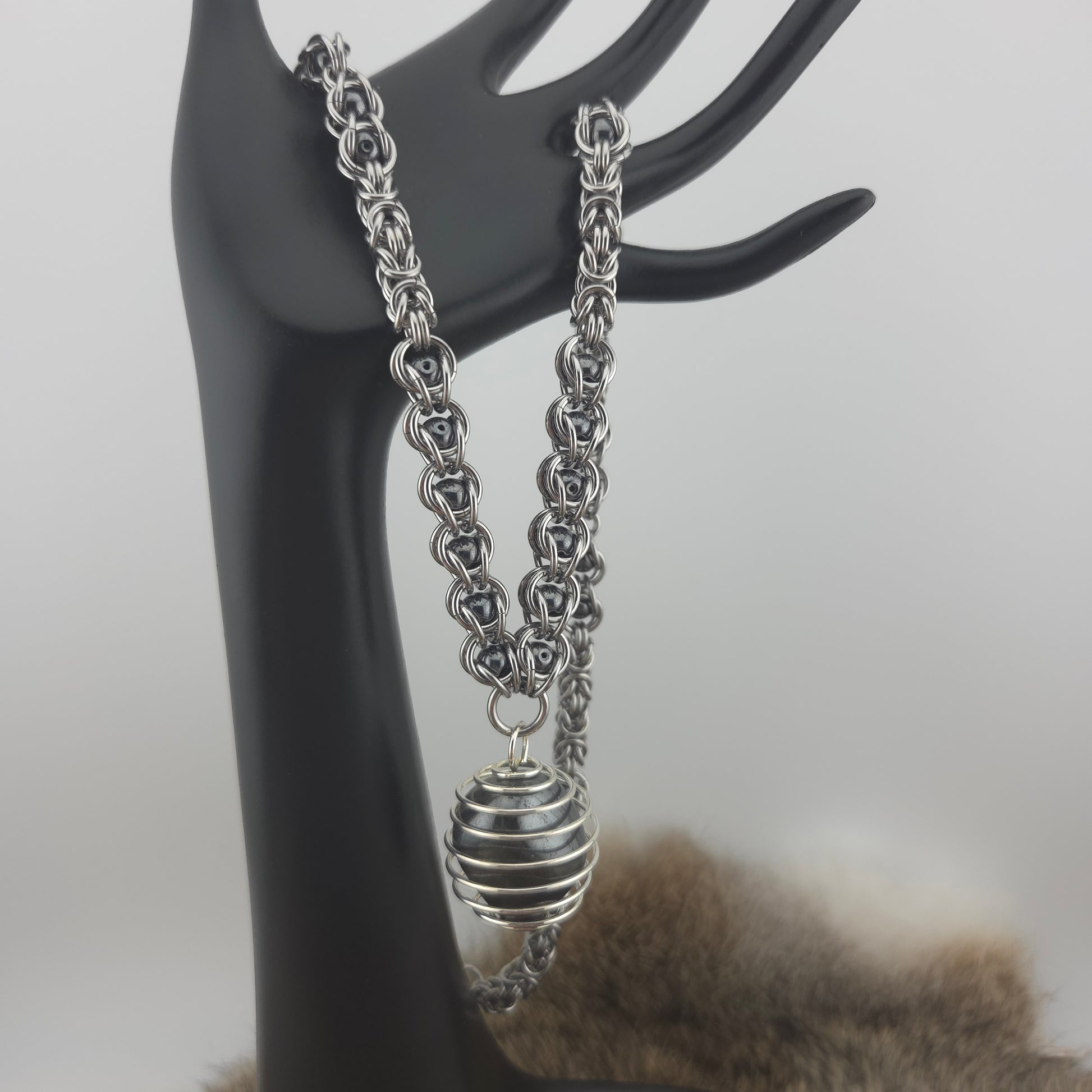 A stainless steel chainmail necklace with a steel spiral wrapped hematite pendant, handwoven.