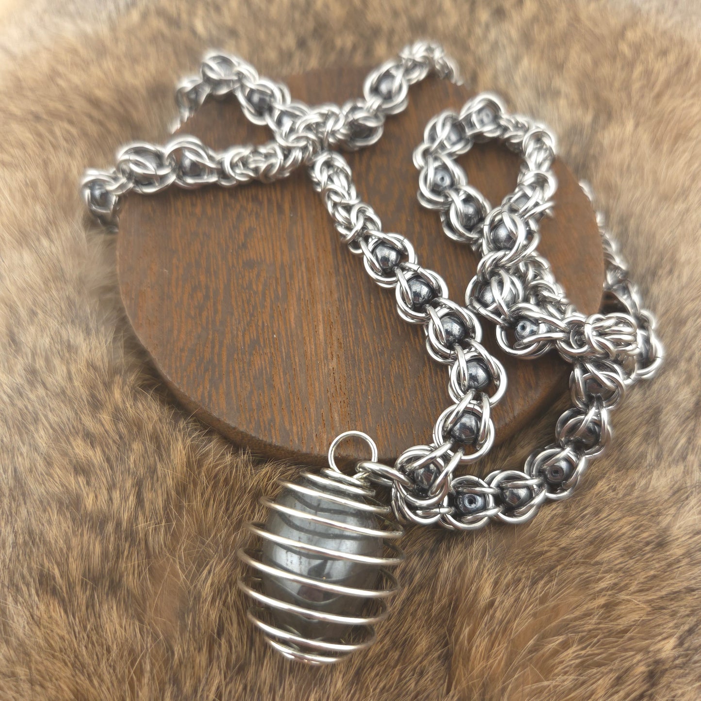 A stainless steel chainmail necklace with a steel spiral wrapped hematite pendant, handwoven.