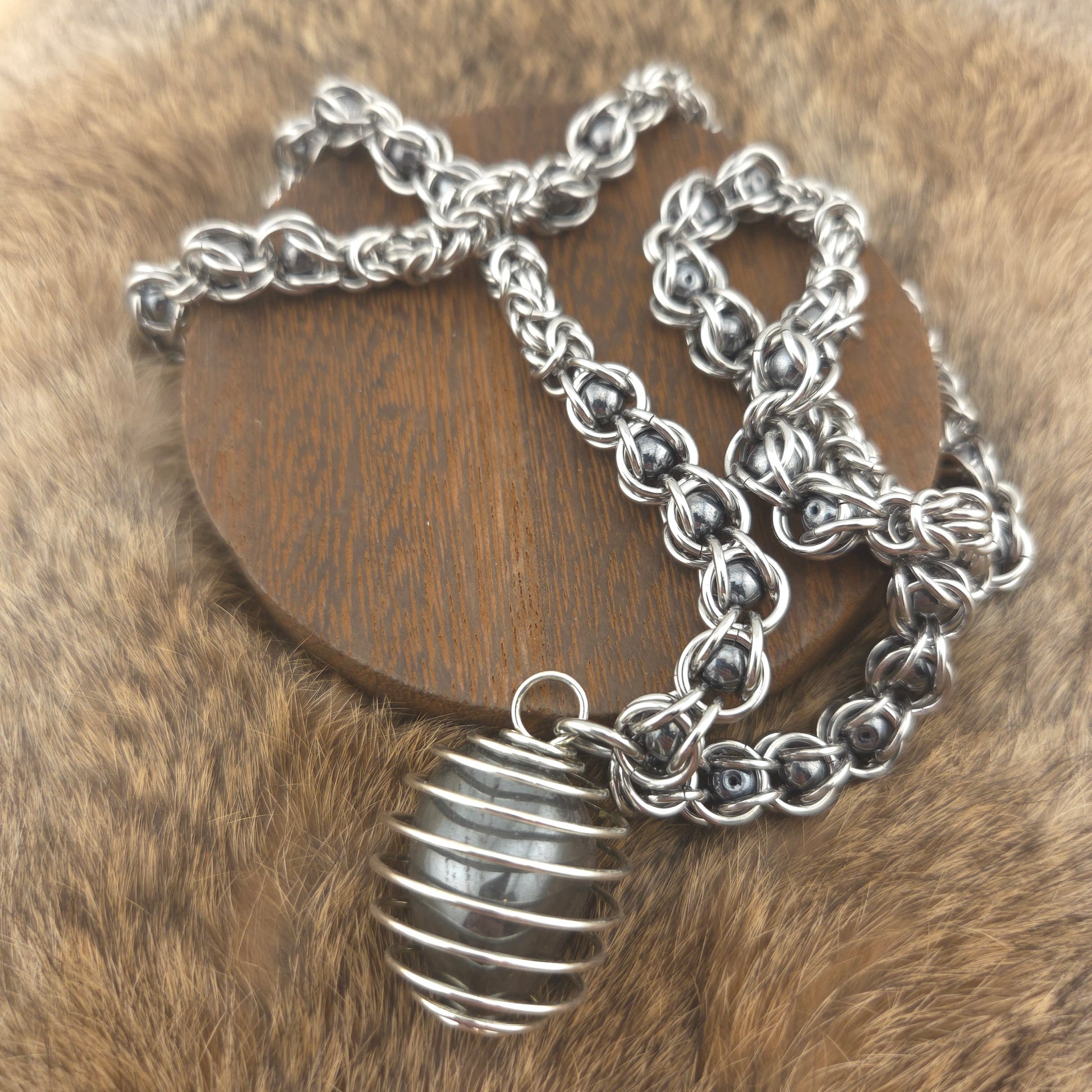 A stainless steel chainmail necklace with a steel spiral wrapped hematite pendant, handwoven.