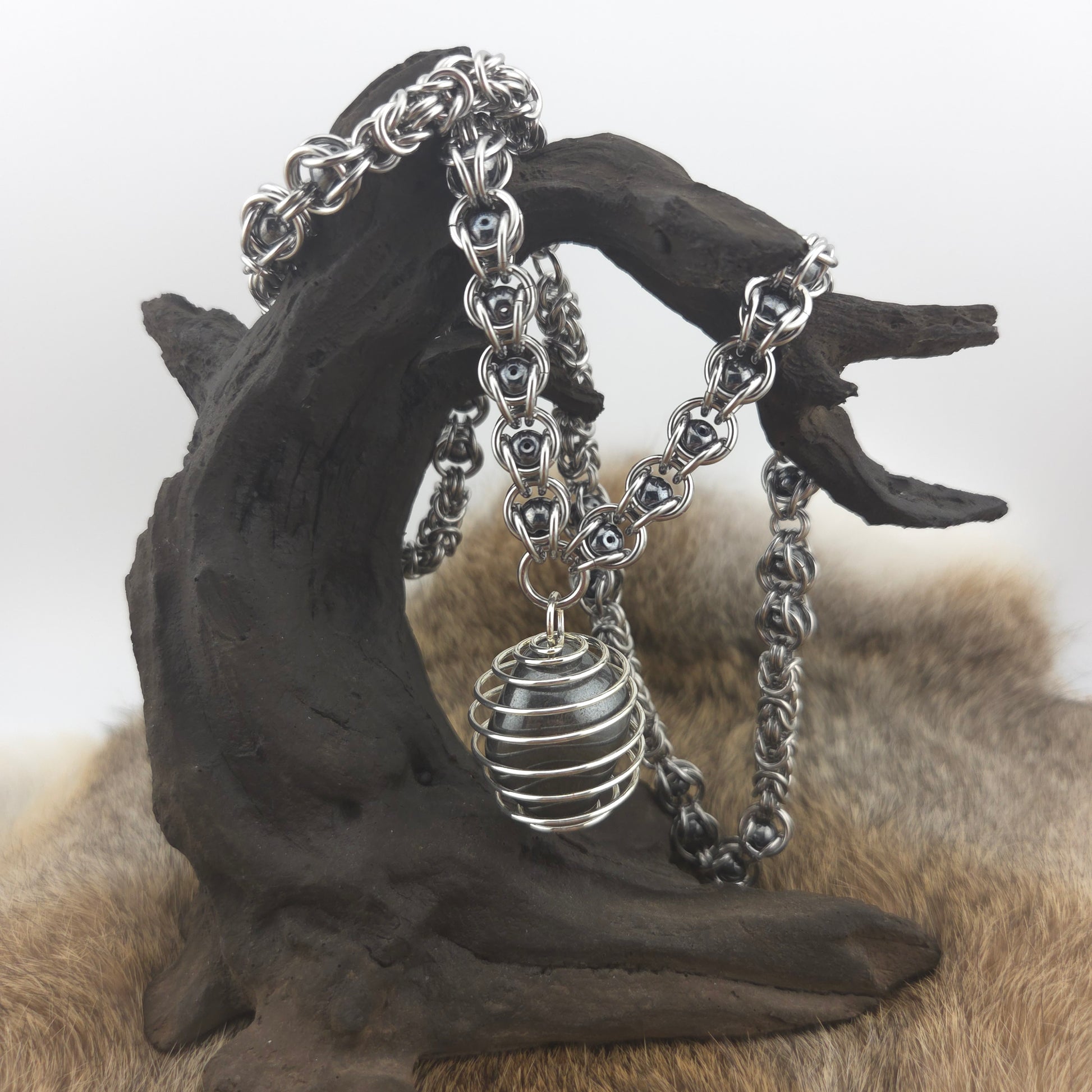 A stainless steel chainmail necklace with a steel spiral wrapped hematite pendant, handwoven.